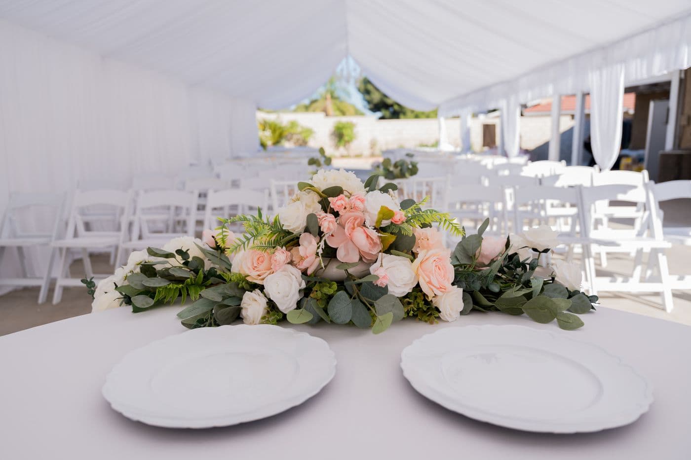 Round banquet table with white linen and place settings under a marquee
